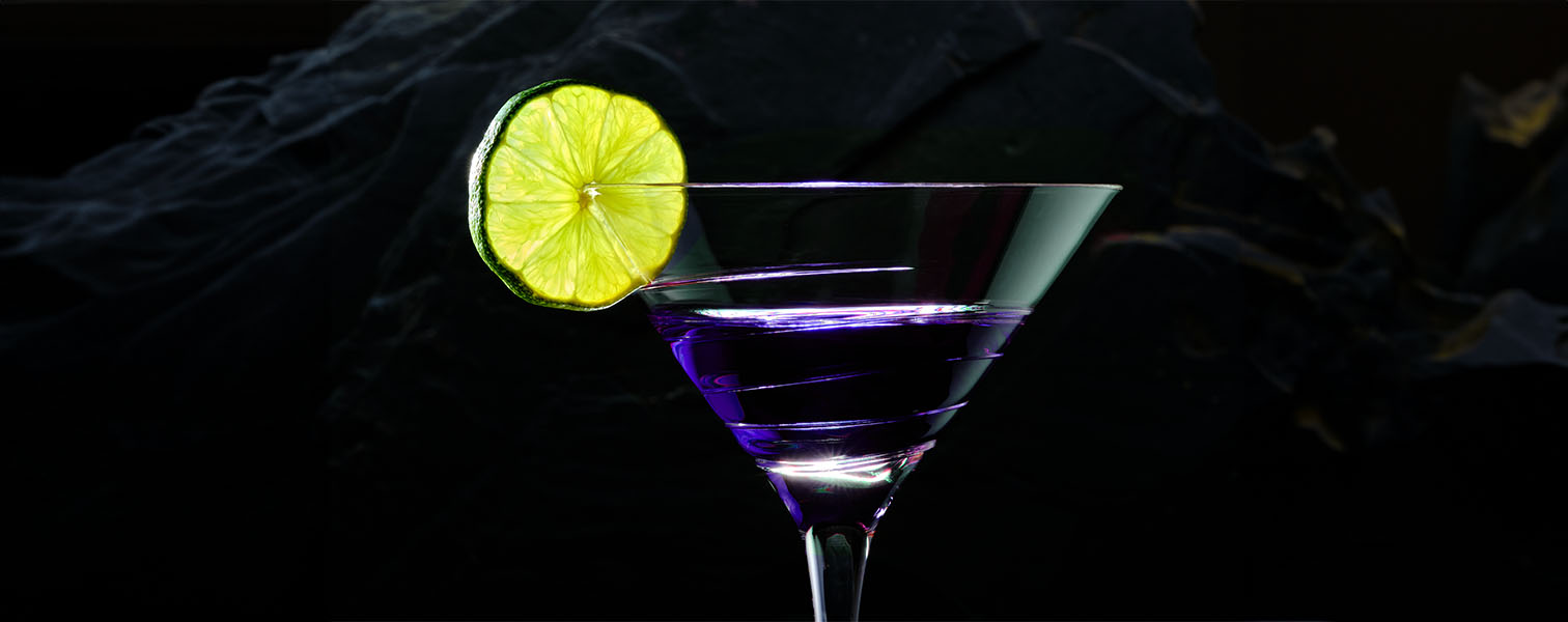 A tall cocktail glass with a lemon on the rim with a black background.