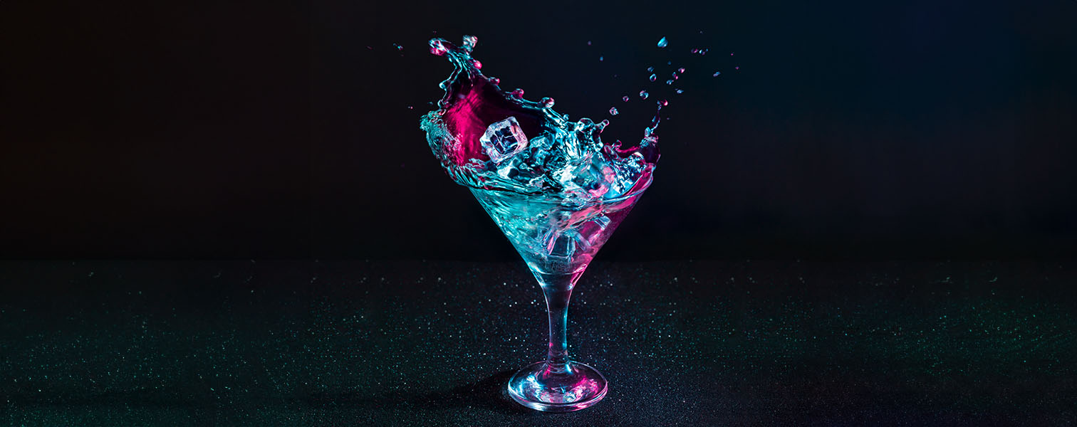 A purple blue ombre drink in a tall cocktail glass with a black background.