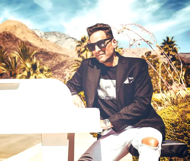 Martin Ross sitting at a white piano with a dessert background.