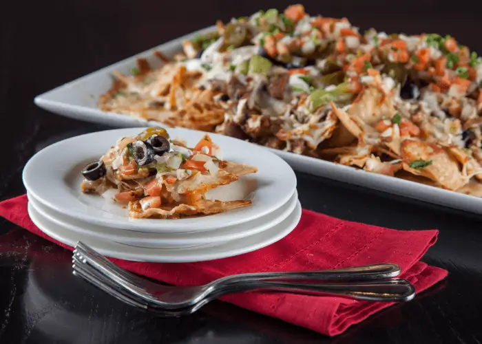 An image of nachos on a tray with a handful on a small stack of plates.